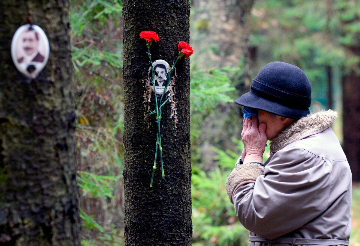 A woman reacts next to a portrait of a victim of Soviet dictator Joseph Stalin's purges at the memorial, where the victims were buried in the woods on the outskirts of Saint-Petersburg, Russia, on Oct. 30, 2017. (Olga Maltseva/AFP via Getty Images)