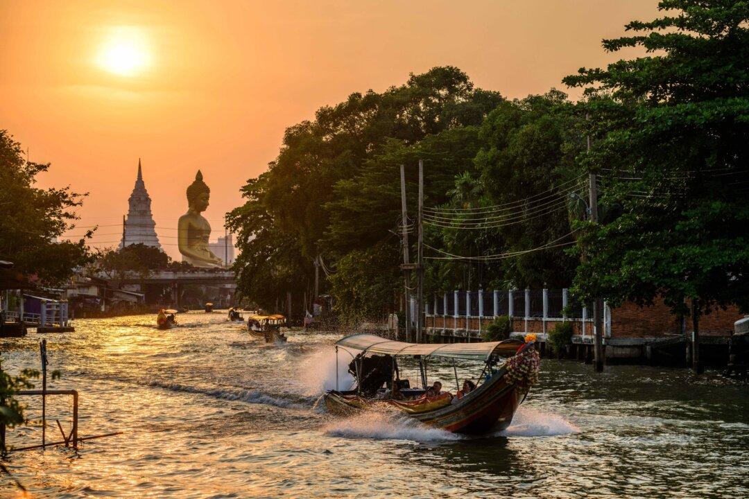 People ride boats in a canal as the sun begins to set behind the 69-meter (226-foot) Buddha statue of Wat Paknam Phasi Charoen temple, in Bangkok on Feb. 16, 2026. (Anthony Wallace/AFP via Getty Images)