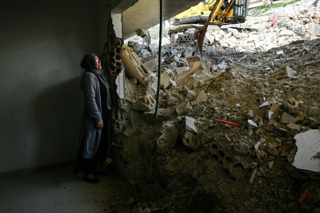 Fatima Al-Nassar, a Palestinian woman living in Lebanon, stands in her damaged apartment as she looks at the rubble of a nearby building that was hit in January by an Israeli strike in the southern village of Qannarit, on Feb. 16, 2026. (Joseph Eid/AFP via Getty Images)