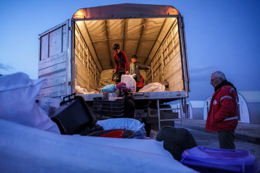 A member of the Syrian Red Crescent society stands by, as children unload items off the back of a truck at the Akbaran camp near Akhtarin, in the north of Syria's Aleppo province, now holding people arriving from eastern Syria, on Feb. 17, 2026. Syria began evacuating remaining residents of Al-Hol camp, which long housed relatives of suspected Islamic State group fighters, as it empties the formerly Kurdish-controlled facility, officials told AFP. (Omar Haj Kadour/AFP via Getty Images)