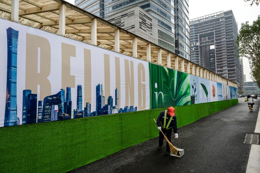 A worker sweeps the road next to a billboard reading “Beijing” in the Central Business District in Beijing on Oct. 18, 2024. Beijing set a 2026 gross domestic product growth target of 4.5 percent to 5 percent—the country’s lowest since 1991. (Kevin Frayer/Getty Images)