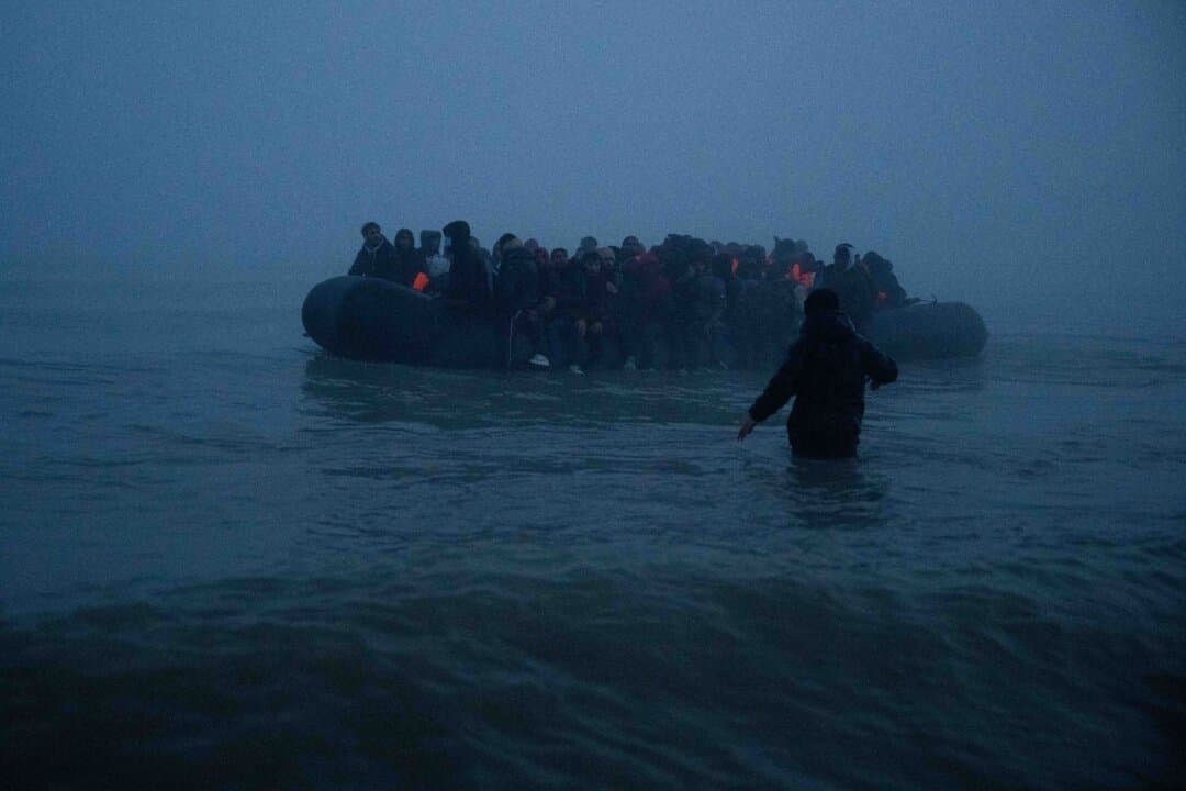 A man wades in the sea to try to board a migrant dinghy to sail into the English Channel in Gravelines, France, on March 4, 2026. Last year the number of people arriving by small boat totaled 41,472, up 13 percent from the previous year, but lower than the 45,774 recorded in 2022. (Carl Court/Getty Images)