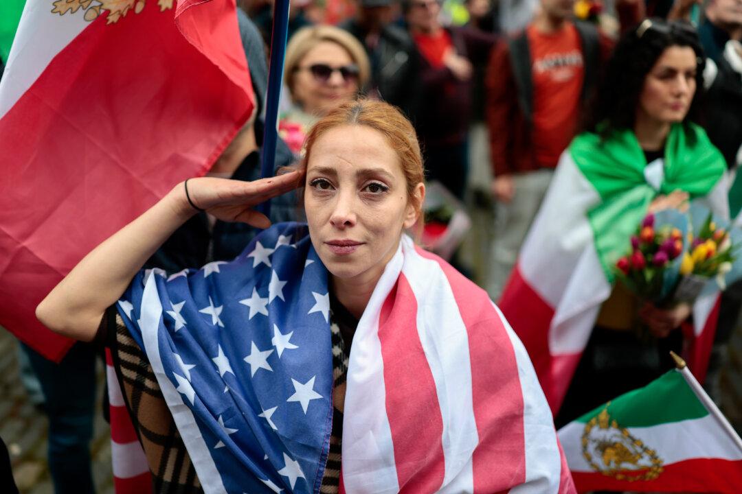 A woman gives a salute gesture while wearing a U.S. flag as Iranians pose with flags and posters outside the U.S. Consulate in Edinburgh, Scotland, on March 5, 2026. (Jeff J Mitchell/Getty Images)