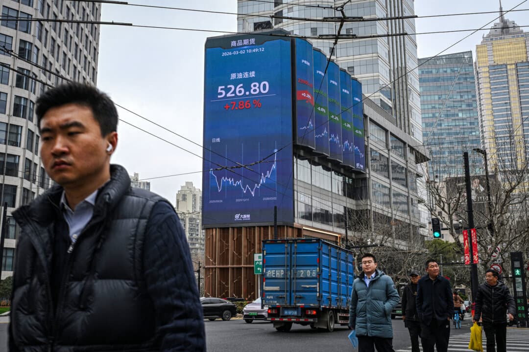 Pedestrians walk next to a screen showing the commodity futures for crude oil in Shanghai on March 2, 2026. Oil prices soared and stocks fell in Asia on March 2 after U.S.–Israeli strikes on Iran sent investors fleeing the prospect of an extended conflict in the crude-rich Middle East. (Jade Gao/AFP via Getty Images)