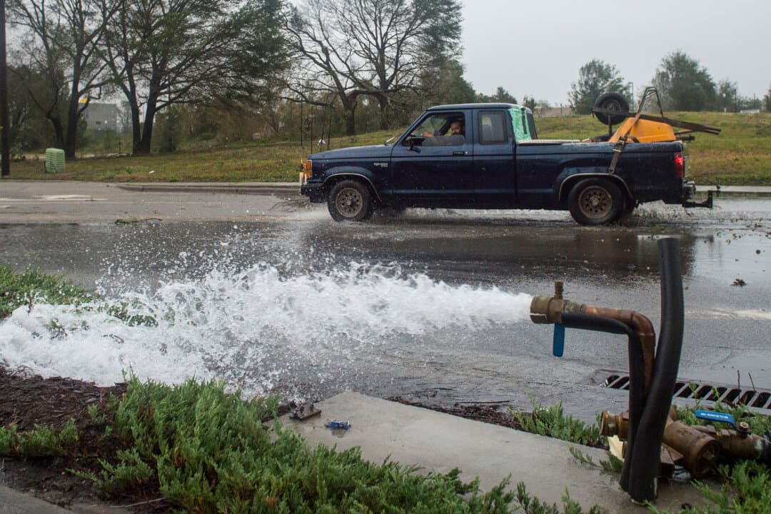A car passes a burst water pipe damaged by strong winds and heavy rain from Hurricane Florence in Wilmington, N.C., on Sept. 14, 2018. Replacing aging water pipes can cost between $1 million and $4 million per mile, depending on pipe size, location, and installation method, according to experts. (Andrew Caballero-Reynolds/AFP via Getty Images)
