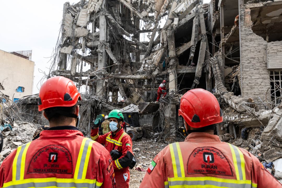 Workers and civilians stand amid the rubble of residential buildings that were destroyed a few days before, following the U.S. and Israeli attack in the eastern Tehran area, in Iran on March 12, 2026. (Majid Saeedi/Getty Images)