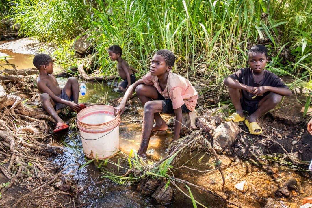 Children sit by a polluted river in the Machinga district, Malawi, on Feb. 20, 2026. Malawian Ministry of Health officials say contaminated water sources like this are a major cause of waterborne disease in the southeastern African nation. (John Fredricks/The Epoch Times)