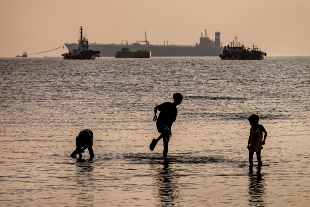 Children play along the shore as the Panamanian-flagged Tiger Wings (L), carrying crude oil from Russia, is seen moored off the Petron oil refinery in Limay, Bataan province, Philippines, on April 1, 2026. (Ezra Acayan/Getty Images)