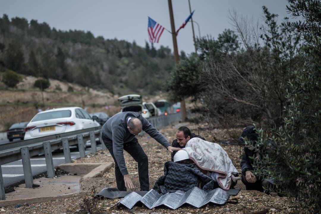 A man holds a helmet on a child as other motorists take shelter in a ditch along a highway during a missile attack in Latrun, Israel, on April 1, 2026. (Marco Longari/AFP via Getty Images)