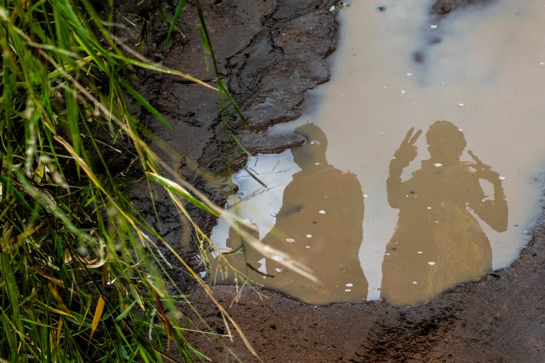 Villagers are reflected in dirty water outside of Mangochi, Malawi, on Feb. 18, 2026. (John Fredricks/The Epoch Times)