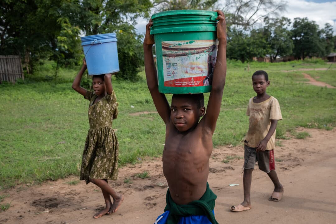Children carry buckets of water in the Mangochi District of Malawi on Feb. 19, 2026. (John Fredricks/The Epoch Times)