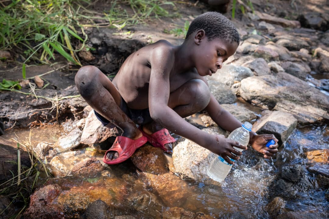 Children drink water from a polluted stream in the Mangochi District of Malawi on Feb. 19, 2026. (John Fredricks/The Epoch Times)