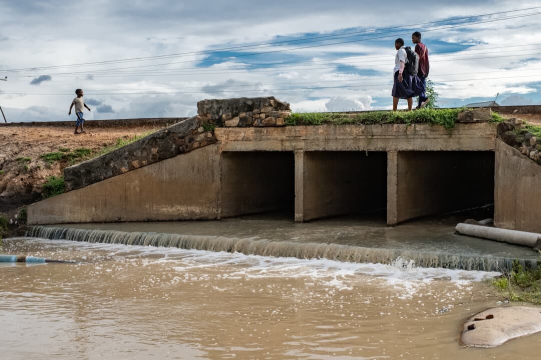 People walk over a polluted water channel outside of Blantyre, Malawi, on Feb. 17, 2026. (John Fredricks/The Epoch Times)
