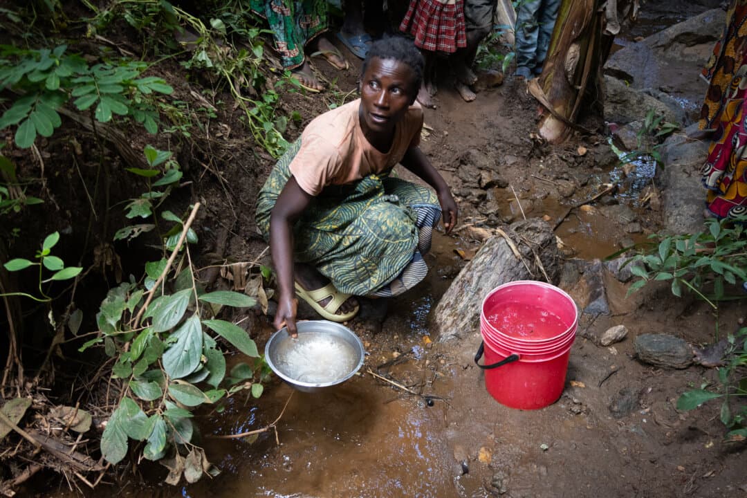 A woman fetches water from a muddy river in the Mwanza District of Malawi on Feb. 24, 2026. (John Fredricks/The Epoch Times)
