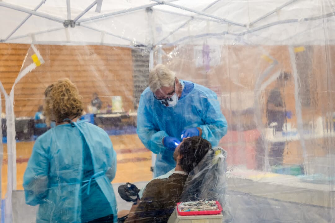 Dentists care for patients at a mobile dental and medical clinic at Terre Haute South High School in Terre Haute, Ind., on Aug. 2, 2025. Nonprofit hospitals are required to demonstrate that they offer financial assistance in various ways that benefit the community, such as educating physicians, conducting health screenings, and providing free medical care through mobile clinics. (Spencer Platt/Getty Images)