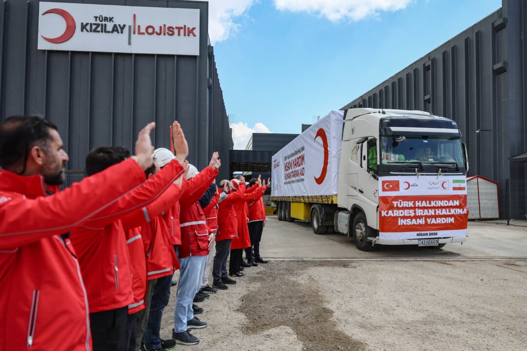Workers wave as a Red Cross and Turkish Red Crescent aid convoy departs Ankara, Turkey, for Iran on April 10, 2026. The groups dispatched emergency humanitarian supplies as officials warned of a desperate situation in Iran. (Adem Altan/AFP via Getty Images)