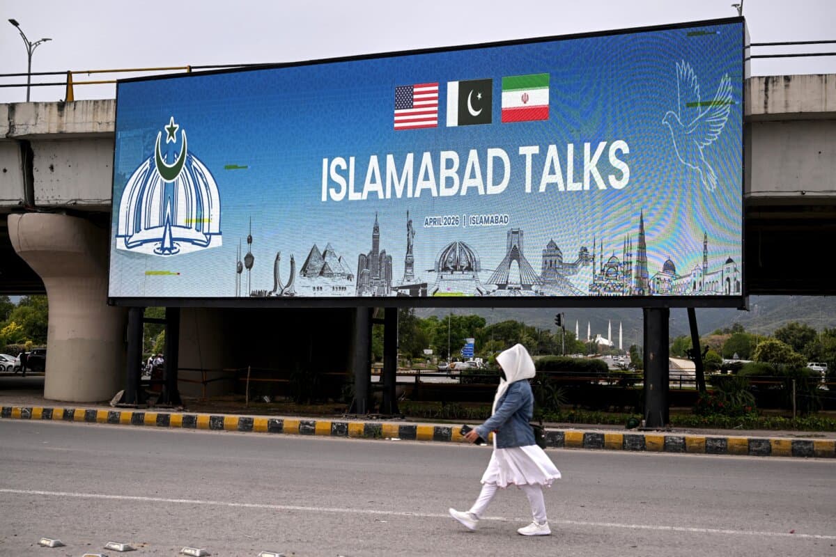 A woman walks past a digital screen displaying news of U.S.–Iran peace talks along a road in Islamabad, on April 10, 2026. (Farooq Naeem/AFP via Getty Images)