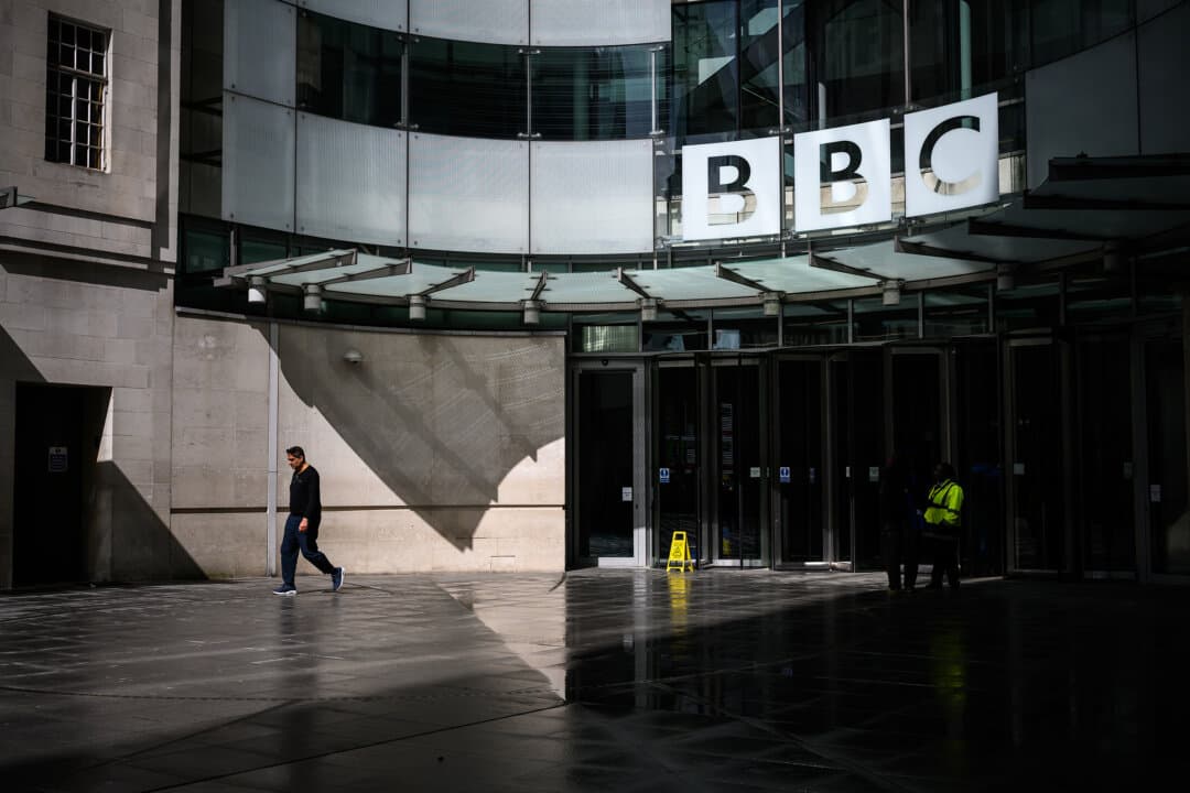 The British Broadcasting Corporation logo is displayed above the main entrance to the BBC's Broadcasting House in London on April 16, 2026. On Wednesday BBC staff were told to expect around 1,800–2,000 jobs to be cut, as the network struggles to lower costs by 10 percent over the next three years. (Leon Neal/Getty Images)