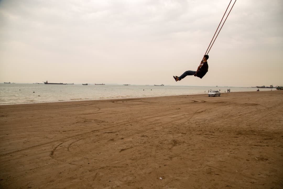 A man enjoys a giant rope swing on the beach as ships are anchored near the shoreline in Bandar Abbas, Iran, on April 22, 2026. (Stringer/Getty Images)
