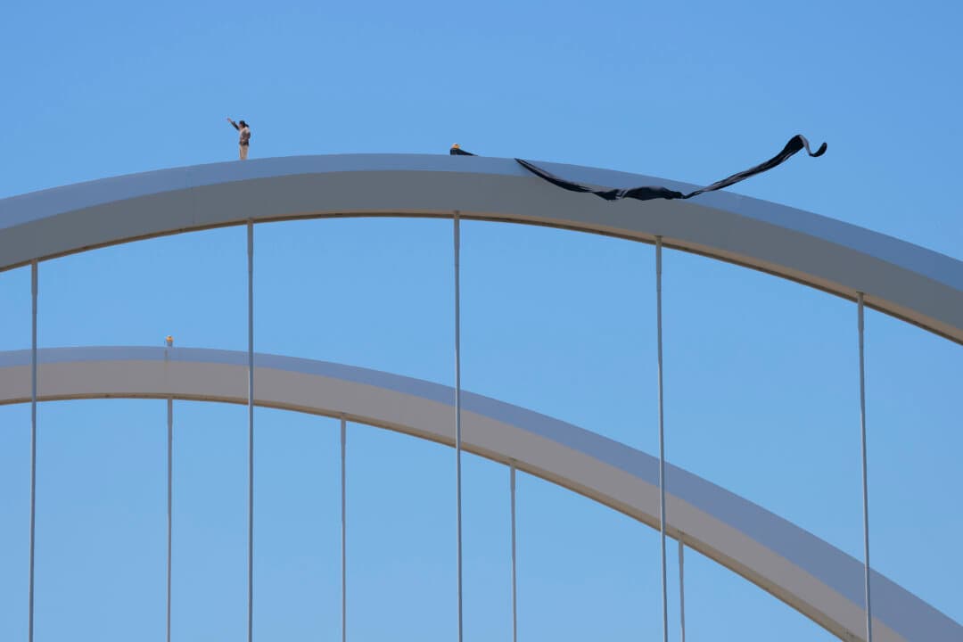 Protester Guido Reichstadter waves to demonstrators below from atop the Frederick Douglass Memorial Bridge in Washington, D.C., on May 5, 2026. Reichstadter climbed the bridge on May 1 to protest the Trump administration’s war in Iran and the development of artificial intelligence, according to posts on X. (Heather Diehl/Getty Images)