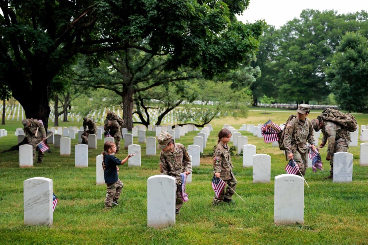 A member of the 3rd U.S. Infantry Regiment, with help from her daughters, places flags in front of each headstone at Arlington National Cemetery in Arlington, Va., on May 21, 2026. (Heather Diehl/Getty Images)
