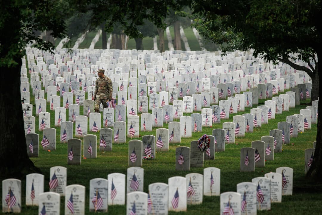 A soldier walks through rows of headstones, placing small American flags in Section 60 at Arlington National Cemetery in Arlington, Va., on May 25, 2026. (Samuel Corum/Getty Images)