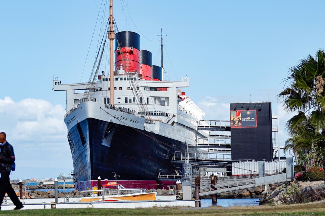 A pedestrian walks near the historic Queen Mary during a celebration in Long Beach, Calif., marking the 90th anniversary of its maiden transatlantic voyage on May 27, 2026. The iconic British Cunard Line ocean liner first set sail from Southampton, England, to New York City on May 27, 1936, and is now permanently anchored in Long Beach. The ship now serves as a floating hotel, museum, and event venue. (Mario Tama/Getty Images)
