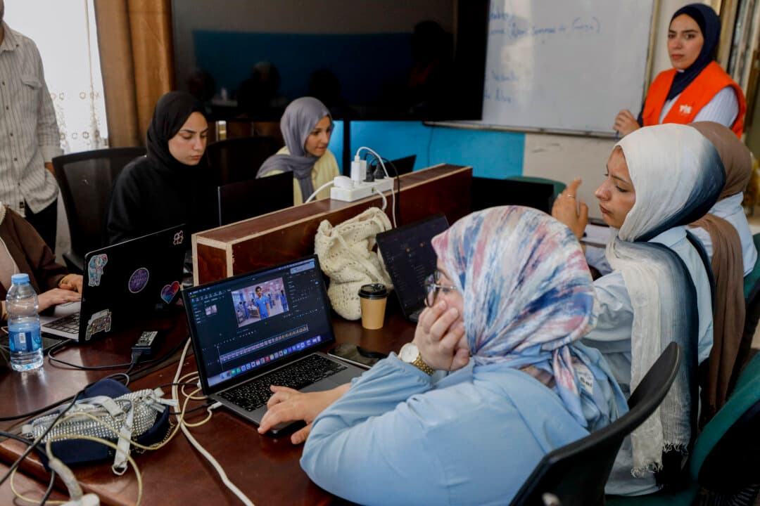 Women sit with laptops around a table during a class in Gaza City, Gaza Strip, on June 1, 2026. The Phoenix Center in Gaza City supports a peer education network that teaches women to use artificial intelligence to document the ongoing war and create alternative income sources. The project aims to develop digital skills and convey local narratives to the outside world. (Ahmed Al Arini/Middle East Images/AFP via Getty Images)