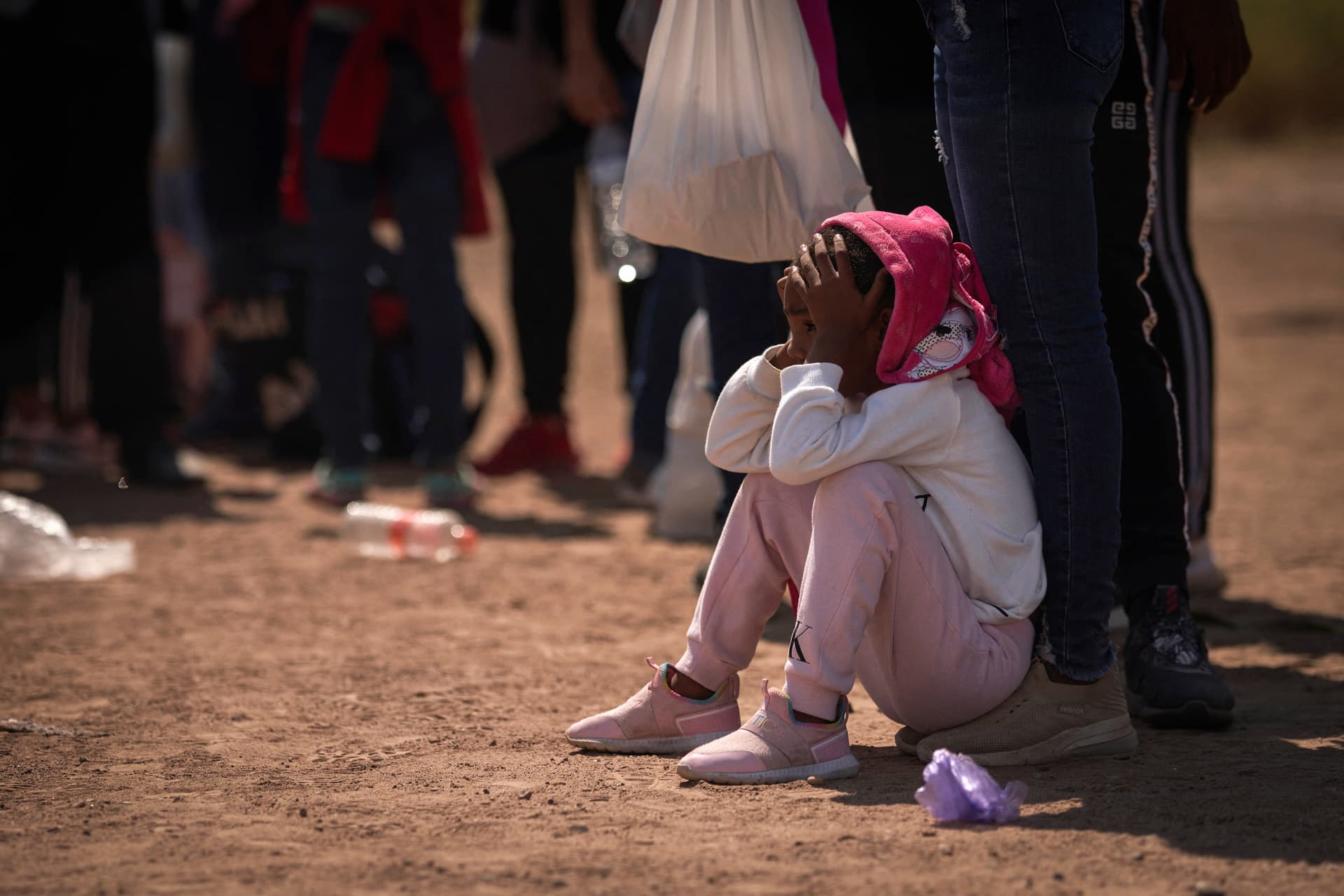 A girl sits on the ground as illegal immigrants wait to be processed by Border Patrol agents, in Eagle Pass, Texas, on Oct. 9, 2022. (Allison Dinner/AFP via Getty Images)