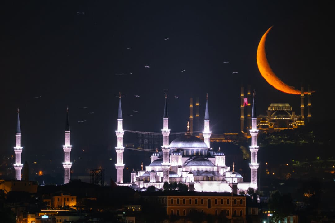 The crescent moon rises behind Sultanahmet mosque (front) and Camlica mosque in Istanbul on June 12, 2026. (Emrah Gurel/AP Photo)