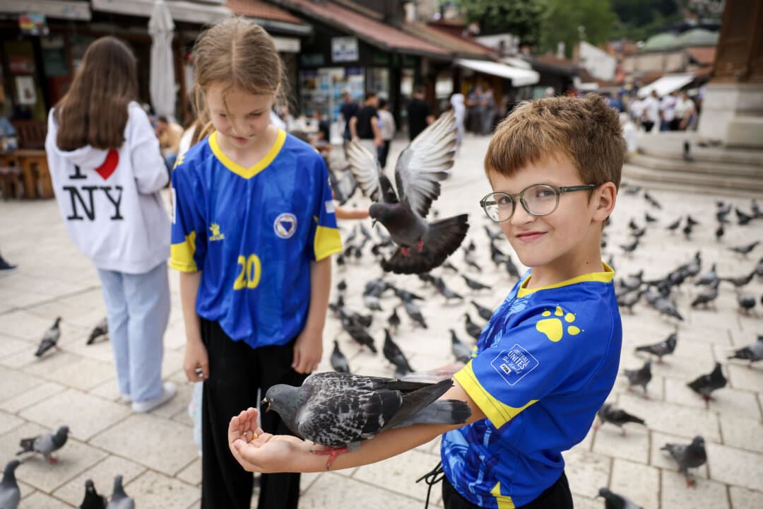 Children in Bosnian national soccer team jerseys feed pigeons in the old part of Sarajevo ahead of the soccer match of the FIFA World Cup 2026 between Canada and Bosnia, in Sarajevo, Bosnia and Herzegovina, on June 12, 2026. (Armin Durgut/AP Photo)