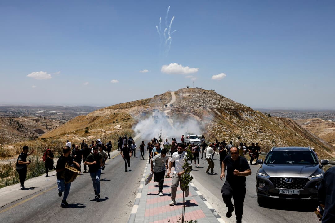 Protesters and local Palestinian landowners, who say some of their land was taken for the newly built Mount Tarousa settlement (background), run from tear gas fired by Israeli security forces blocking a road leading to the hilltop during a rally against the settlement near Dura in the West Bank on June 19, 2026. (Hazem Bader/AFP via Getty Images)