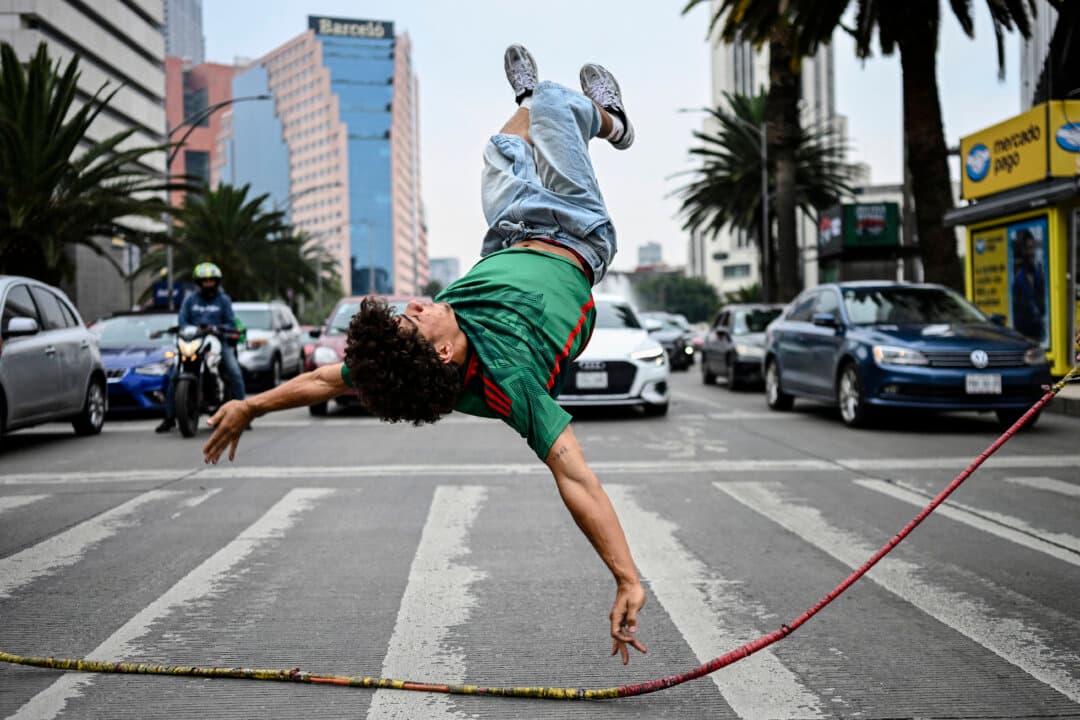 A Venezuelan immigrant performs an acrobatic move while jumping a rope held by two companions as they collect money from drivers waiting at a traffic light in Mexico City, Mexico, on June 19, 2026. (Yuri Cortez/AFP via Getty Images)