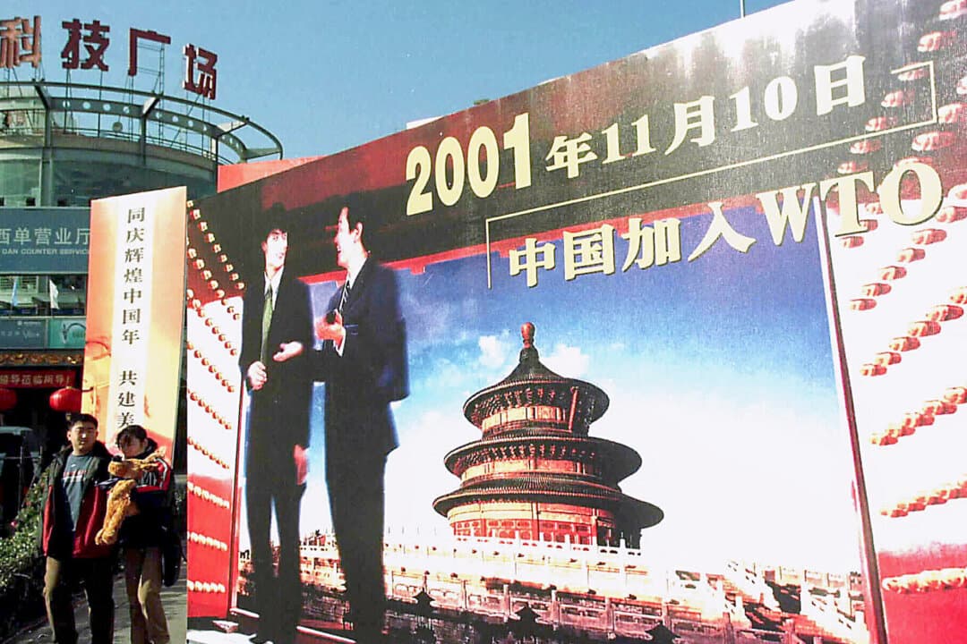 People walk past a billboard celebrating China's 2001 entry to the World Trade Organization, in Beijing on Jan. 5, 2002. Living standards rose in China as the Chinese Communist Party opened the country to Western capital, technology, and markets. (AFP via Getty Images)