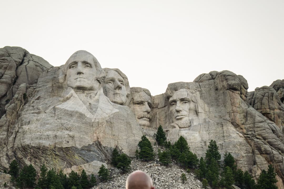 A motorcyclist looks at Mount Rushmore National Memorial, also known as the Shrine of Democracy, depicting Presidents George Washington, Thomas Jefferson, Theodore Roosevelt, and Abraham Lincoln, in Keystone, S.D., on Aug. 3, 2025. Construction of the monument was so dangerous, “it’s astonishing that no one was killed,” historian Ben Jones said. (Madalina Kilroy/The Epoch Times)