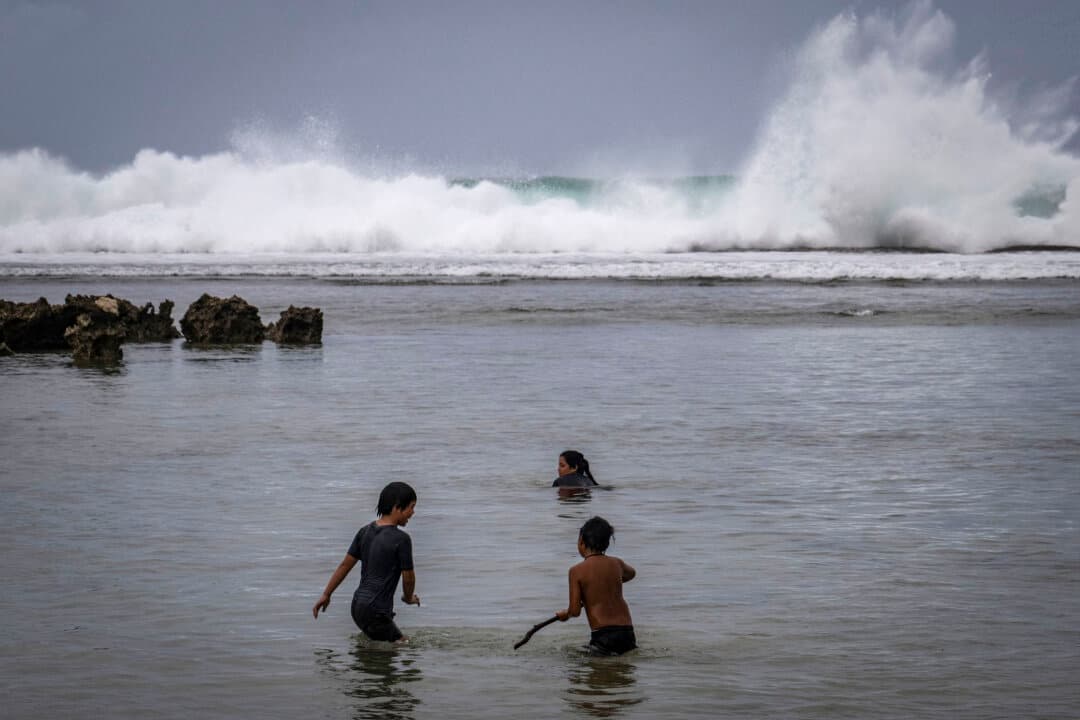 Waves hit the coastline as children play at a beach ahead of the arrival of the forecasted Super Typhoon Bavi in Guam on July 4, 2026. (Yuichi Yamazaki/AFP via Getty Images)