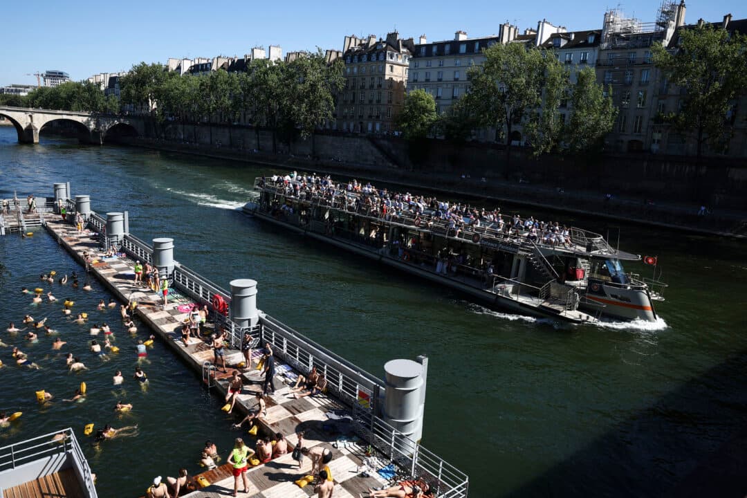 A tourist boat sails past swimmers bathing at the Bras Marie safe bathing site on the opening day of the swimming areas on the Seine river, in Paris, on July 4, 2026. (Romain Perrocheau/AFP via Getty Images)