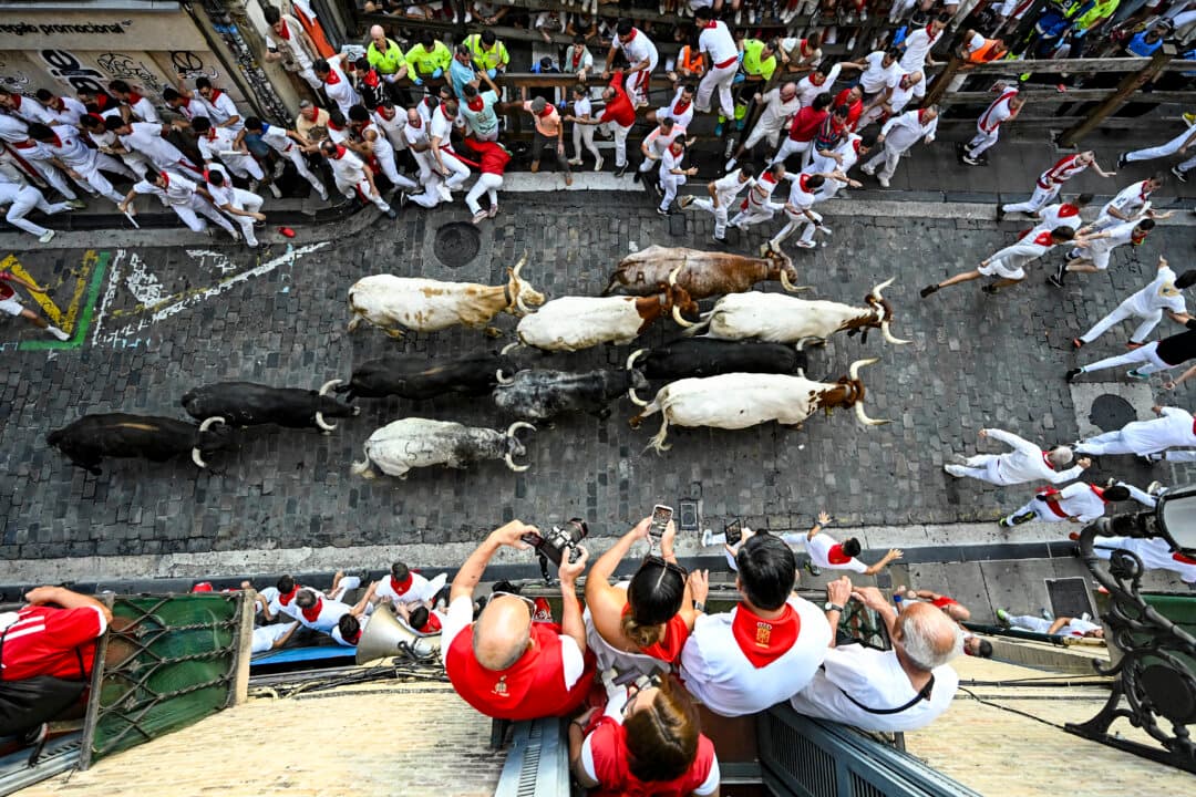 People watch from a balcony as participants run ahead of bulls from the Cebada Gago bull ranch during the second running of the bulls of the San Fermin festival in Pamplona, Spain, on July 8, 2026. (Ander Gillenea/AFP via Getty Images)