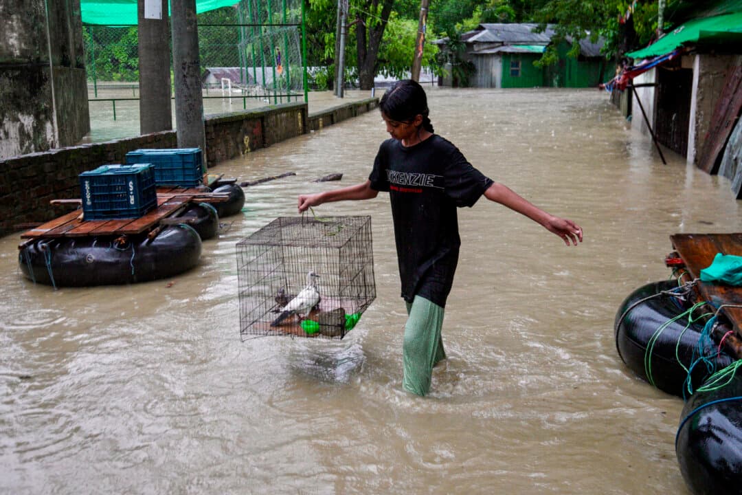 A girl carrying pet birds wades through a flooded area following heavy rains in Bandarban, Bangladesh, on July 8, 2026. (Syed Amir Hosain Masum/AFP via Getty Images)