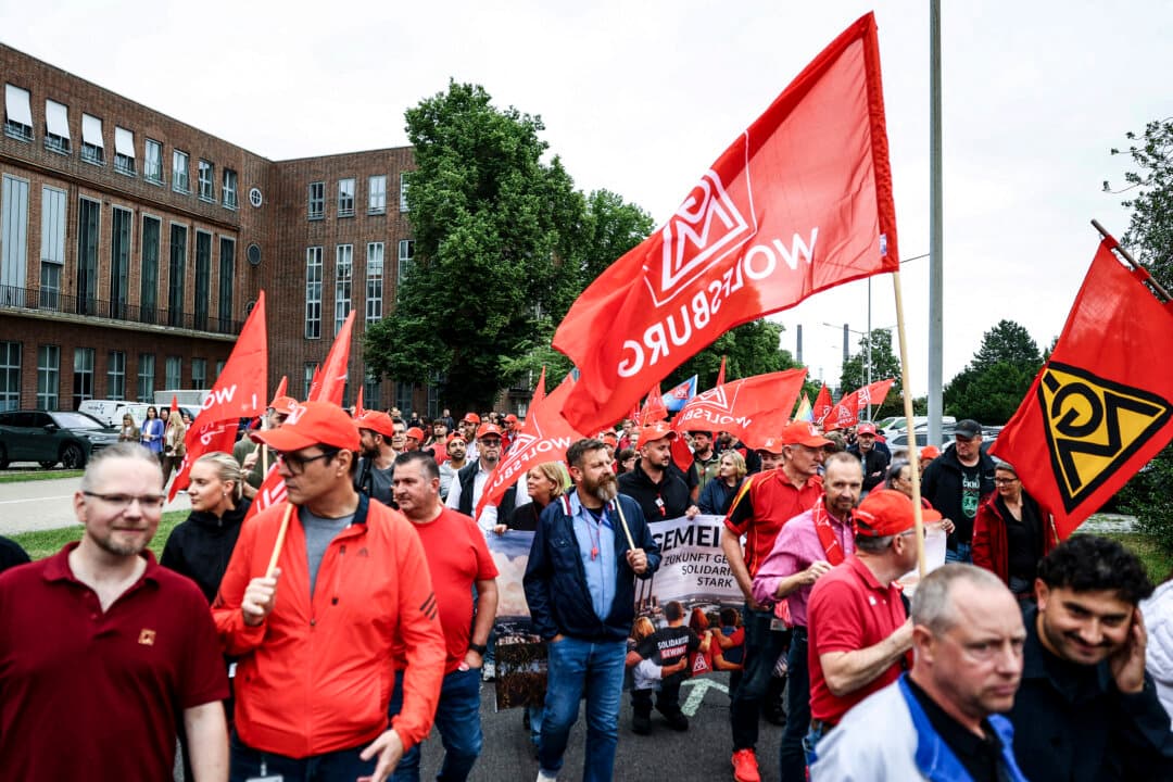 Employees of Volkswagen, Europe's largest carmaker, carry flags of German trade union IG Metall at a rally to protest planned restructuring and massive job cuts at the VW headquarters in Wolfsburg, Germany, on July 9, 2026. (Lisi Niesner/Pool/AFP via Getty Images)