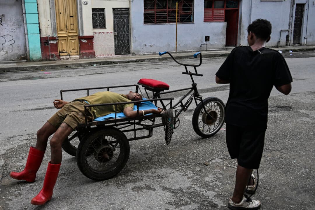 A man rests on a cargo tricycle as another person walks past in Havana, Cuba, on July 11, 2026. (Yamil Lage/AFP via Getty Images)