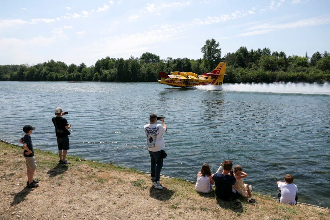 Local residents take photos as a Canadair CL-415 of the French civil security performs water-scooping maneuvers by skimming across the Seine river in Chartrettes, in Paris' Ile-de-France region, on July 13, 2026, following the forest fire in Fontainebleau Forest. (Thomas Samson/AFP via Getty Images)