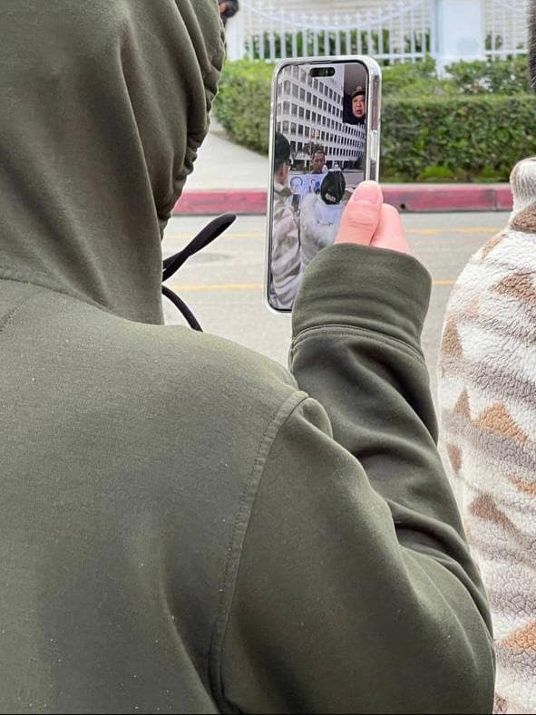 A hooded man livestreams Jie Lijian during a protest outside the Chinese Consulate in Los Angeles in December 2022. The phone screen shows a Chinese man wearing a police uniform on the other end of the call. (Courtesy of Jie Lijian)