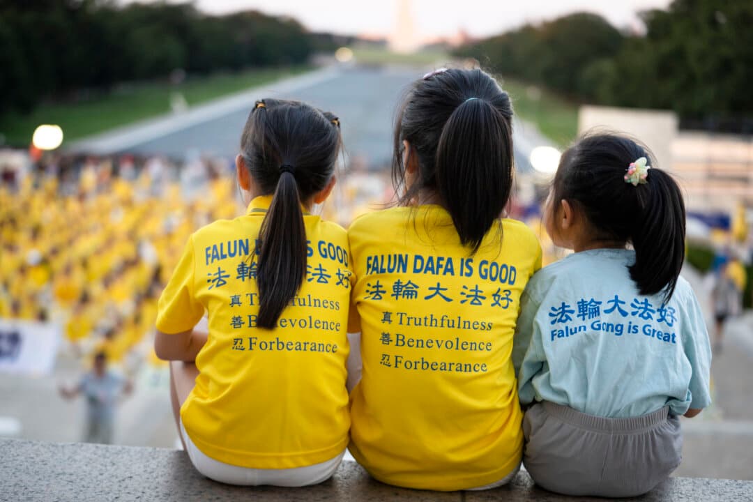 Three young Falun Dafa practitioners sit together on the steps of the Lincoln Memorial in Washington on July 23, 2026. (Madalina Kilroy/The Epoch Times)