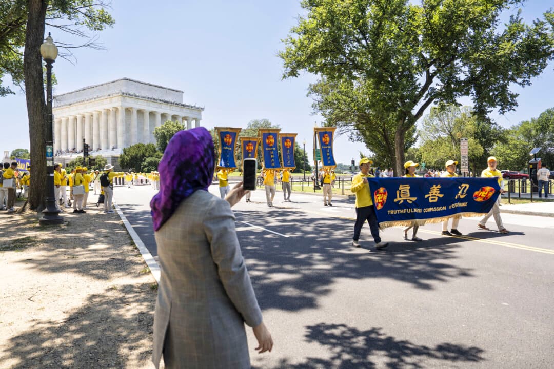 A passerby takes videos of Falun Dafa practitioners in Washington on July 23, 2026. (Madalina Kilroy/The Epoch Times)