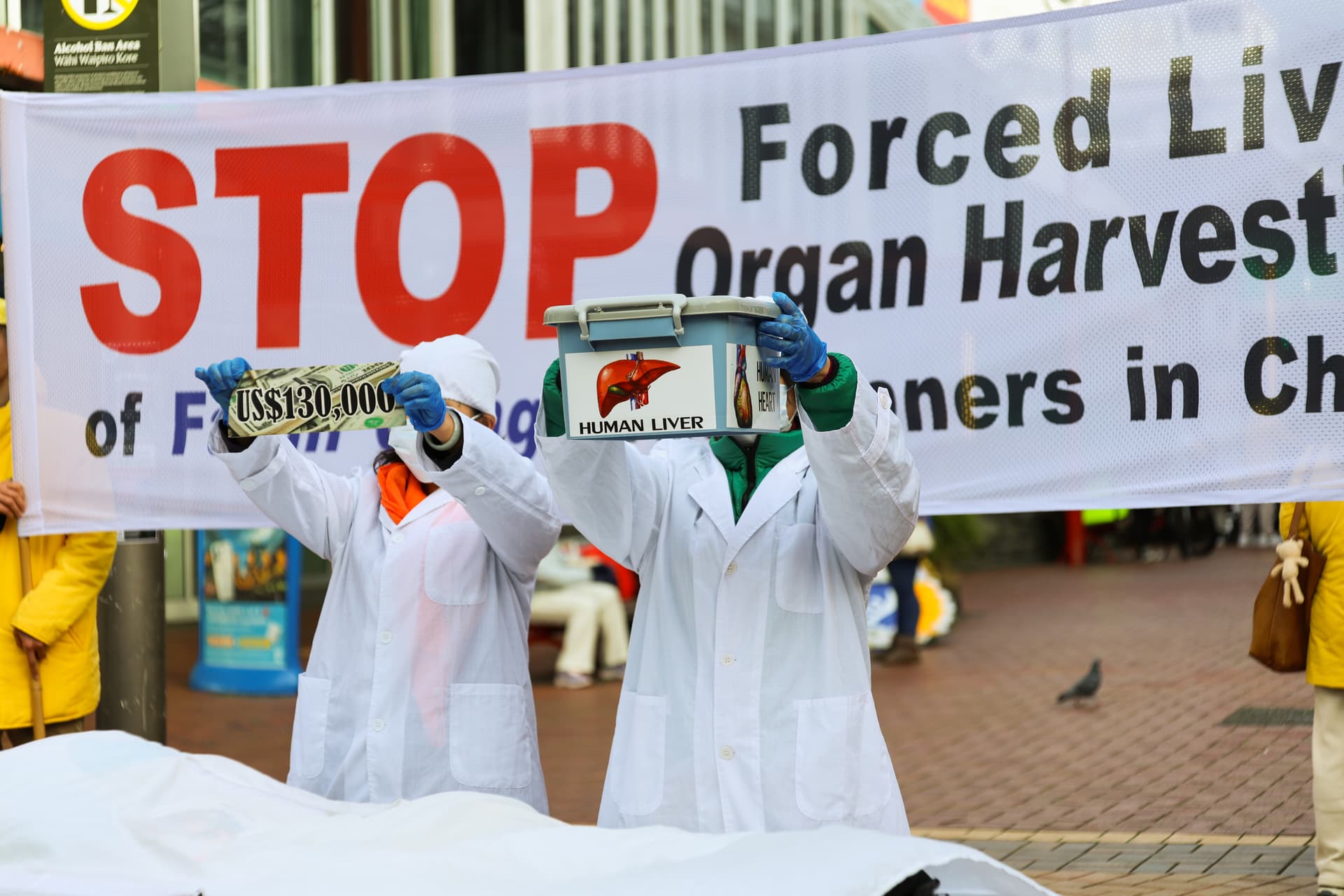Advocates stage a dramatic reenactment in lab coats to raise awareness and demand an end to forced organ harvesting in China during a rally in Wellington, New Zealand, on July 21, 2026. (Echo Wang/The Epoch times)