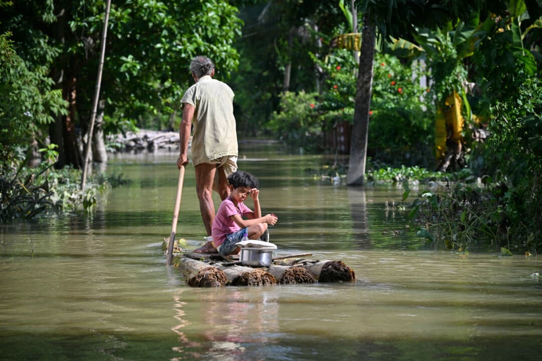 A girl and her grandfather travel on a raft through floodwaters following heavy monsoon rains in Sivasagar district, India, on July 27, 2026. (Biju Boro/AFP via Getty Images)