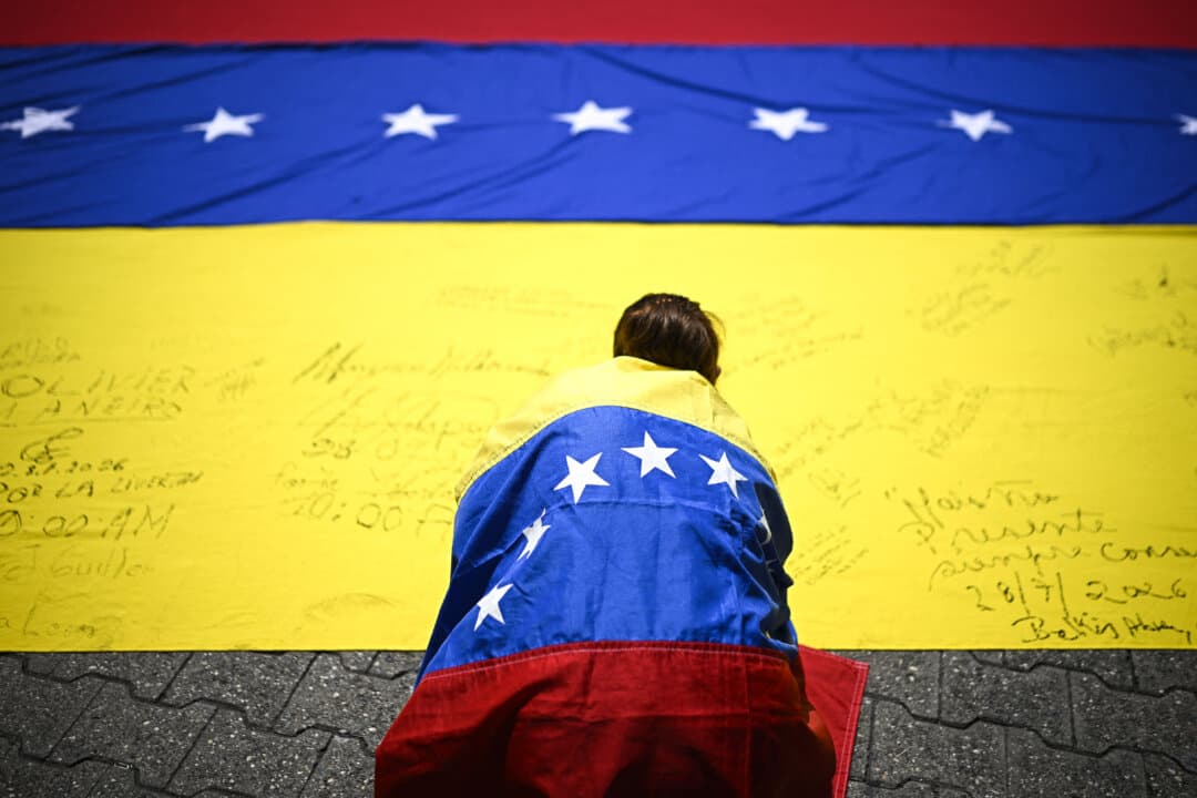 A unionist wrapped in a Venezuelan national flag signs another Venezuelan flag during a protest march calling for elections in Caracas, Venezuela, on July 28, 2026. (Federico Parra/AFP via Getty Images)