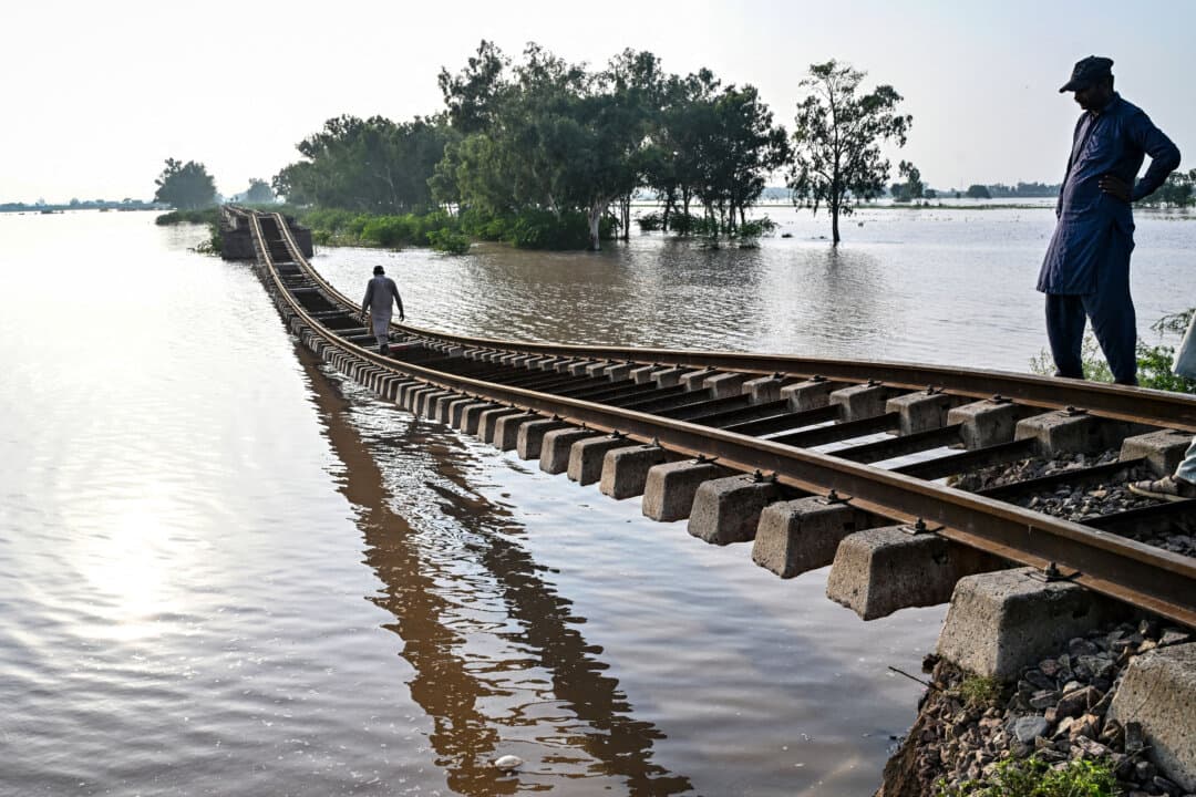 People walk over a damaged railway track in a flooded area after the Ravi River overflowed following heavy monsoon rains, in Sheikhupura, Pakistan, on July 29, 2026. (Arif Ali/AFP via Getty Images)