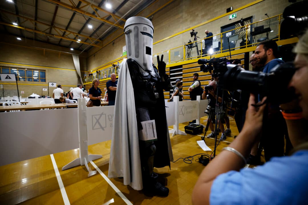 Jon Harvey, dressed as the satirical character Count Binface, poses for the press at Clacton Leisure Centre as election workers review ballots after voting closed in the Clacton-on-Sea By-election in Clacton-on-Sea, England, on Aug. 14, 2026. The Clacton-on-Sea by-election was triggered by Reform UK leader Nigel Farage resigning his seat to seek voter approval amid parliamentary scrutiny over an undeclared million-pound donation from a Crypto billionaire. In protest of what they called a political stunt, the main UK parties have boycotted the race, leaving 33 opponents consisting of independents and fringe candidates. (Dan Kitwood/Getty Images)